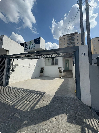 Fachada da Inata Quiropraxia e Bem-Estar com logo na parede e portão aberto para estacionamento.