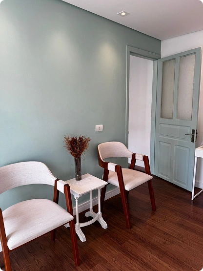 Poltrona branca com estrutura em madeira ao lado de uma mesinha com vaso decorativo.